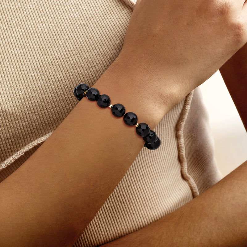Onyx bead stretch bracelet on wrist, dark faceted beads with yellow gold spacer accents