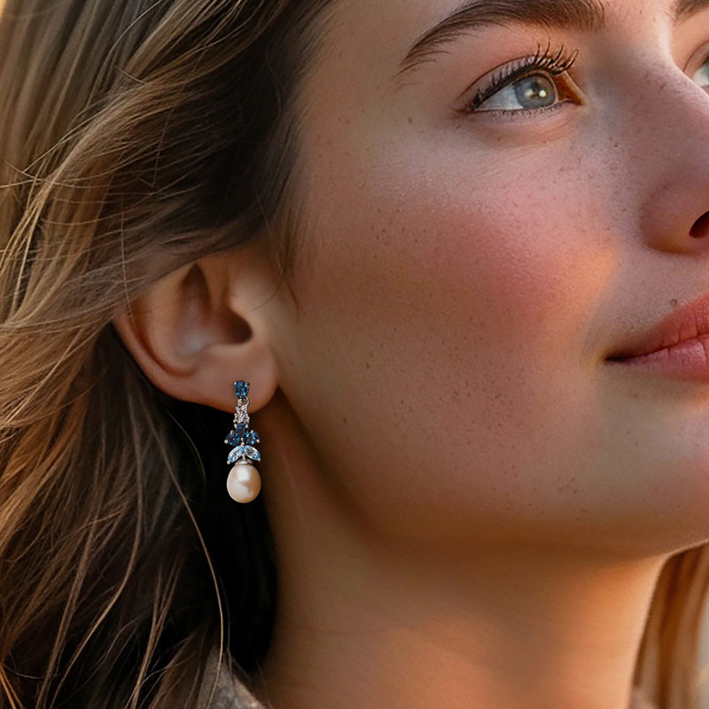 Cultured pearl drop earrings with blue topaz clusters, worn on model's ear