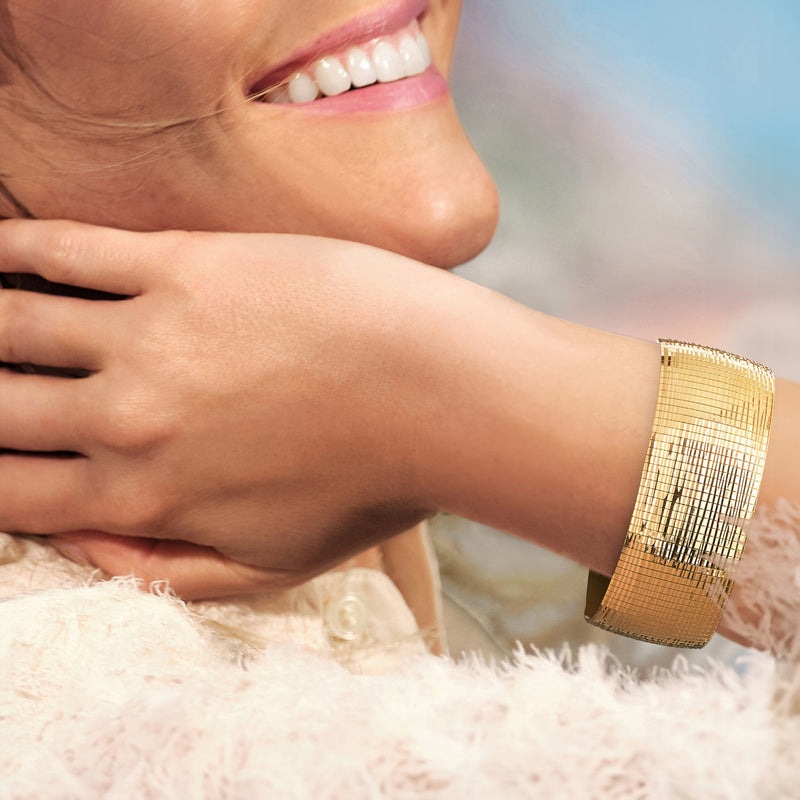 Gold omega bracelet on wrist, diamond-cut mesh texture with polished edges.