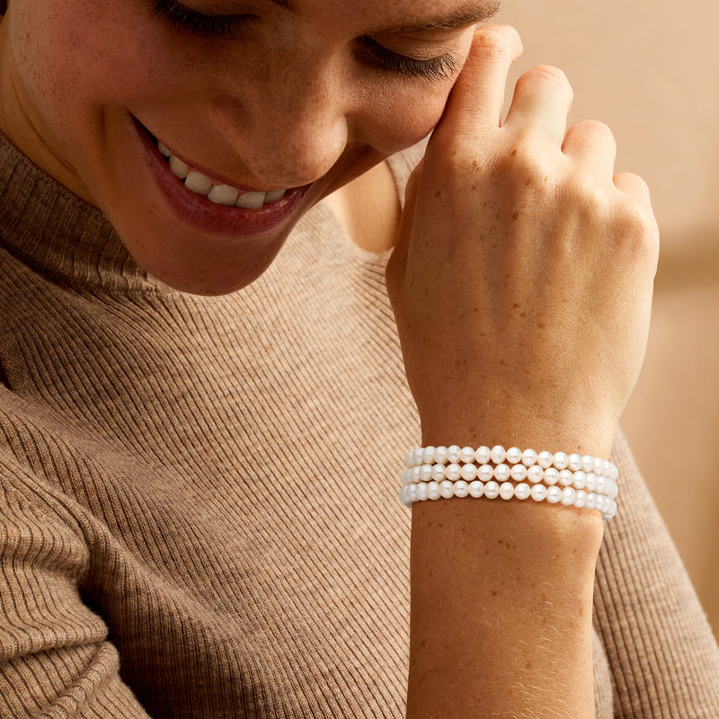 Cultured pearl three-strand bracelet worn on wrist, white round pearls with silver clasp