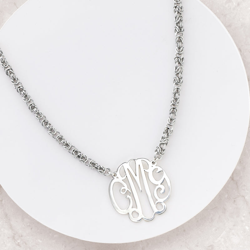 Sterling silver monogram necklace with ornate pendant and curb chain on stand