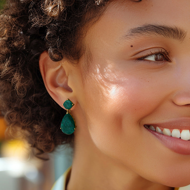 Emerald drop earrings worn on ear, emerald-green stones with gold-tone settings