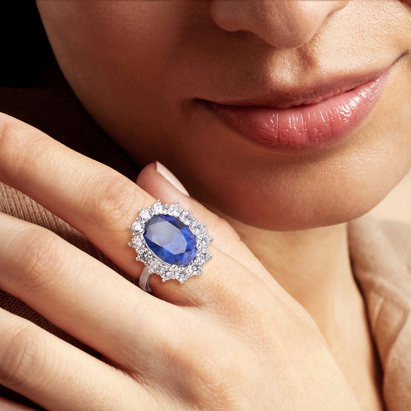 Sterling silver oval blue ring with CZ halo worn on finger, close-up