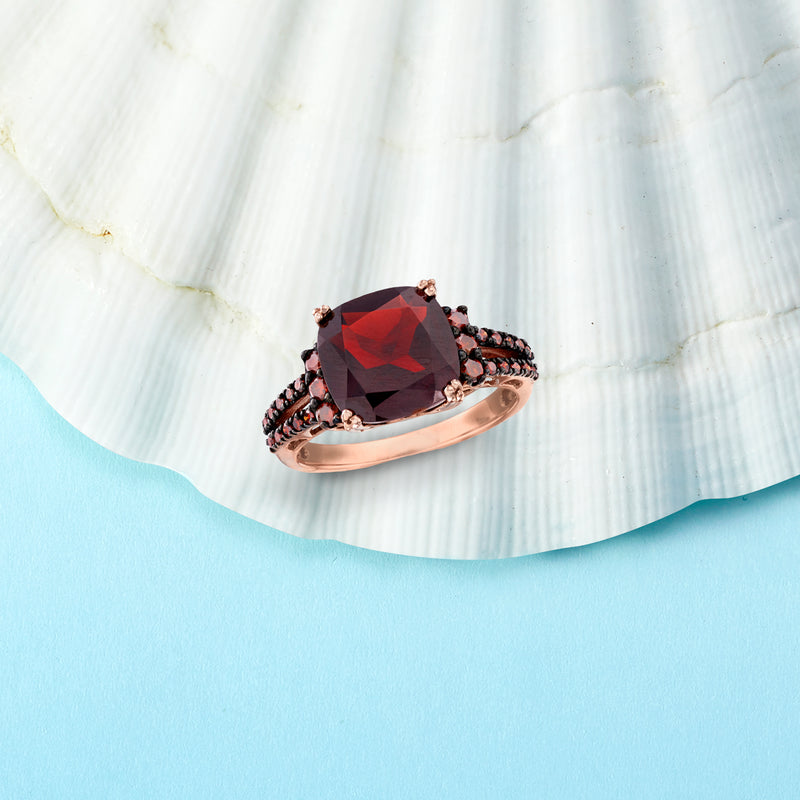 Rose gold ring featuring red oval garnet center with black-toned side stones