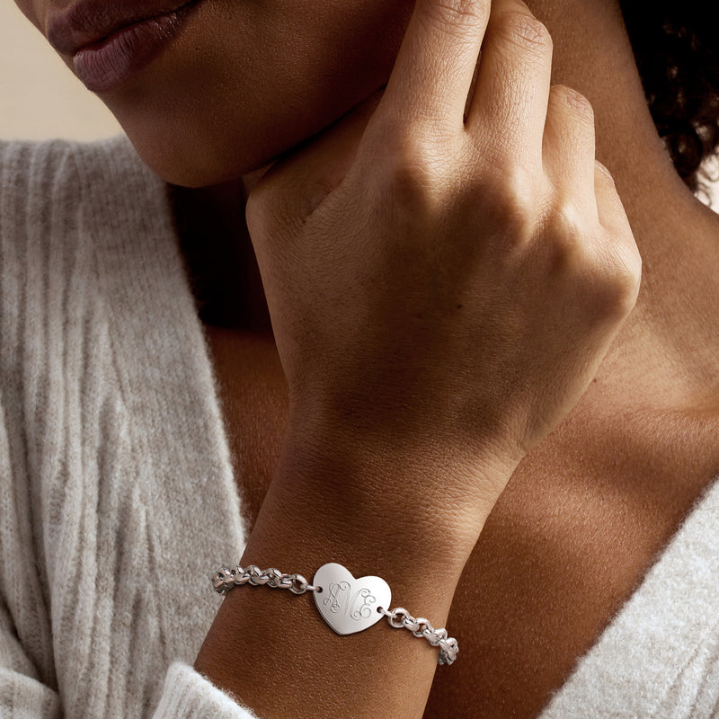 Sterling silver heart charm bracelet worn on wrist; engraved monogram heart.