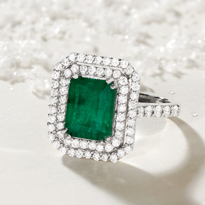 Close-up diamond halo ring with emerald-cut green center, white gold