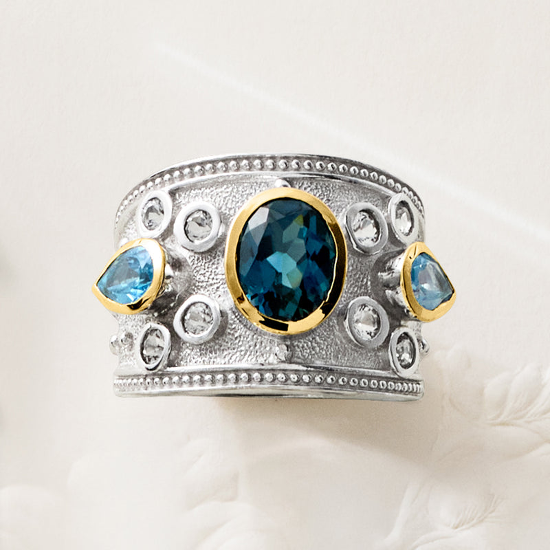 Sterling silver dome ring with oval deep blue centerpiece, blue accents, and halo detailing