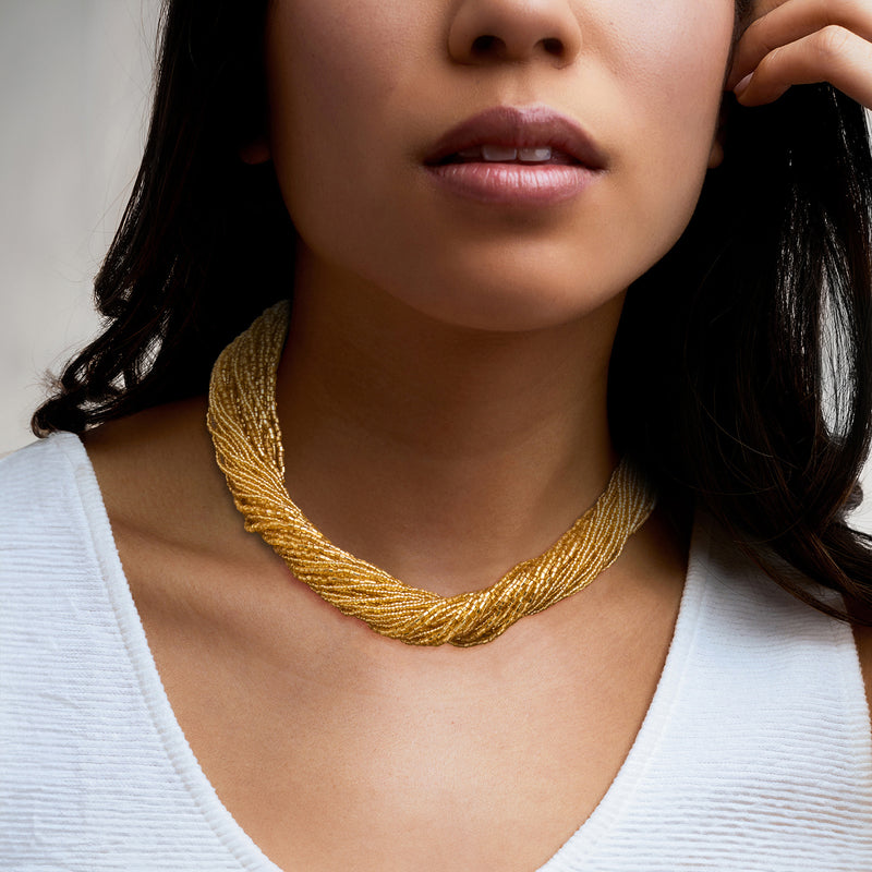 Golden bead torsade necklace worn with white top, three-strand twisted look