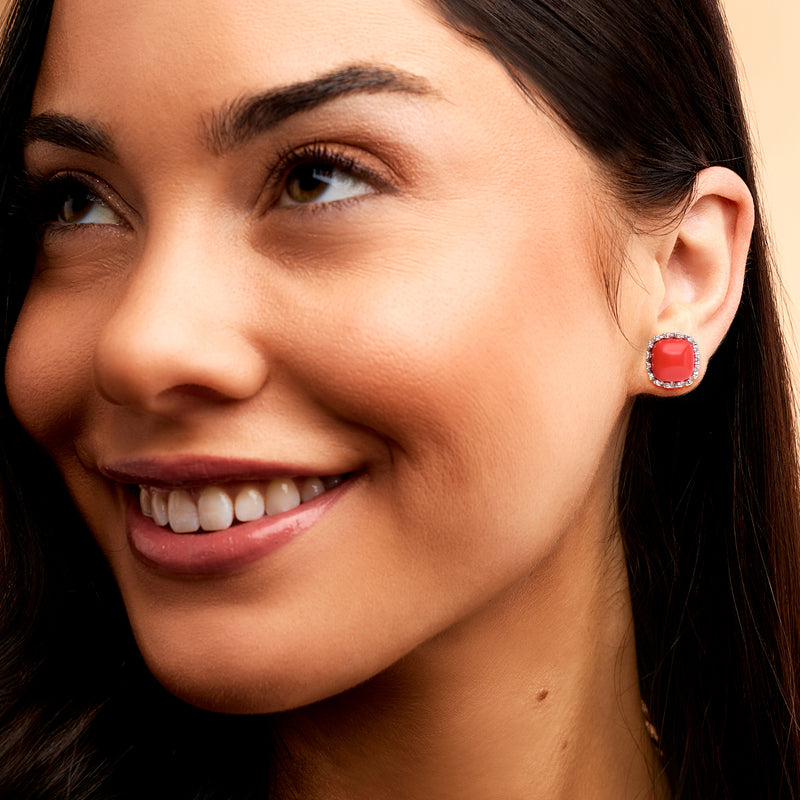 Coral red cushion stud earrings on model’s ear with silver halo border