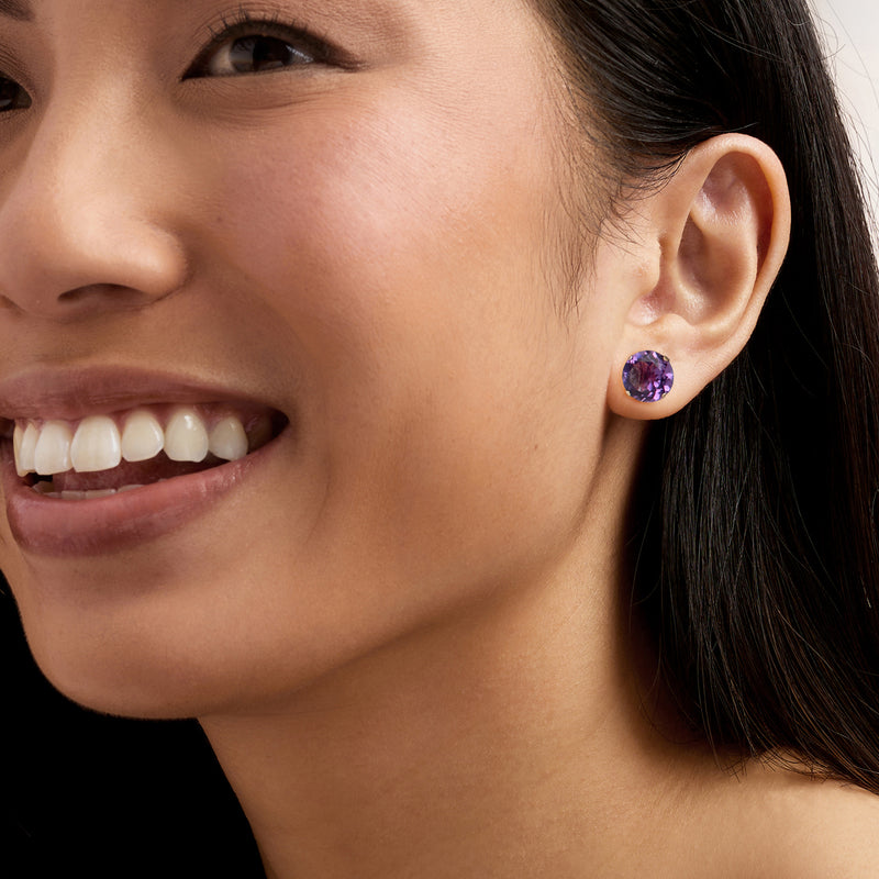 Amethyst stud earring on ear: round purple gemstone with 14kt yellow gold prongs