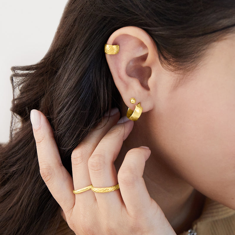 Small yellow gold huggie hoop earrings on ear, polished hinged design
