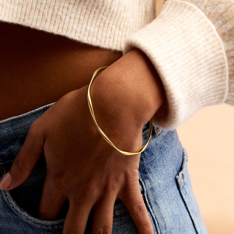 14kt yellow gold twisted bangle bracelet worn on wrist, polished cuff