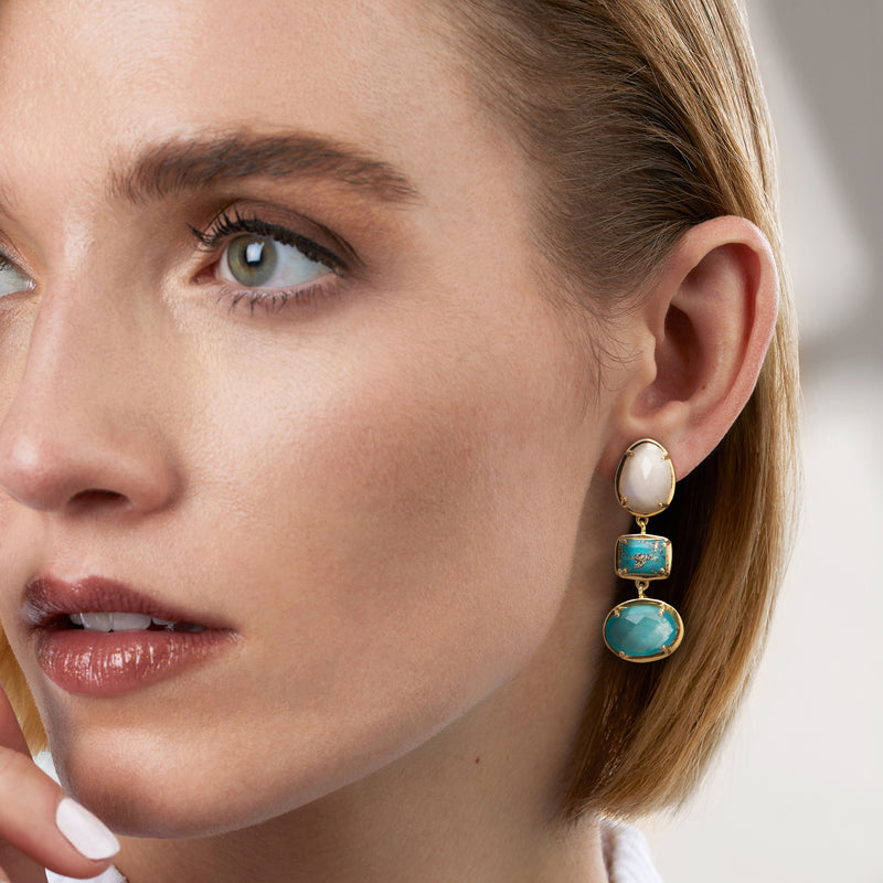 Gold drop earrings with white moonstone and teal square-and-oval gemstone drops on ear