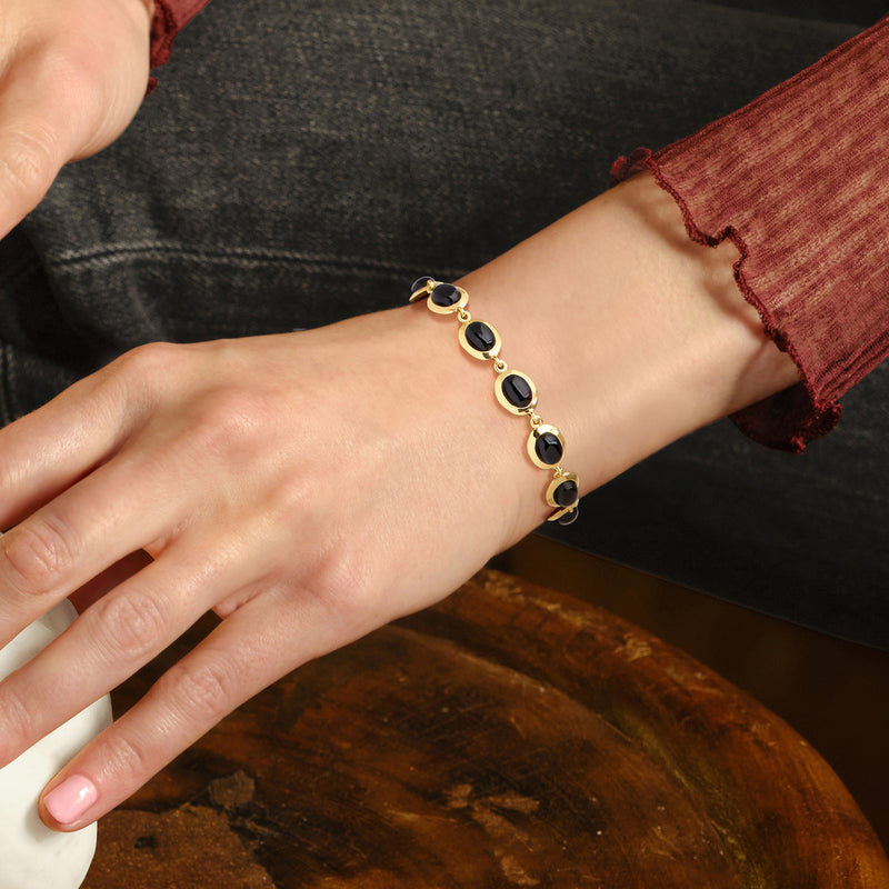 Gold-tone bracelet with black oval cabochons worn on wrist, chain and clasp visible