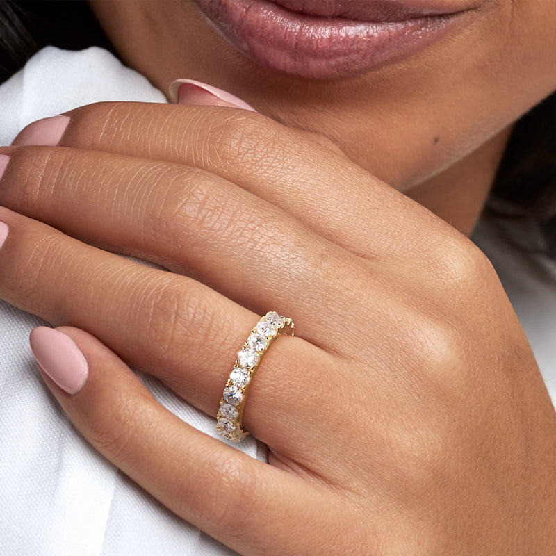 Diamond eternity band on finger in 14kt yellow gold, close-up of round stones