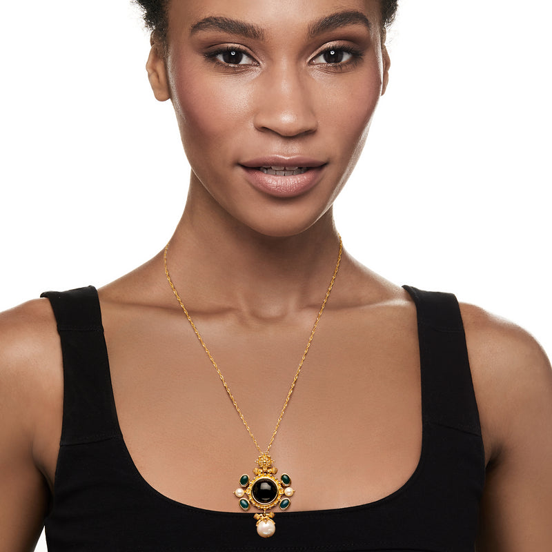 Gold-tone pendant necklace worn at neckline: black center with green accents and pearl drop