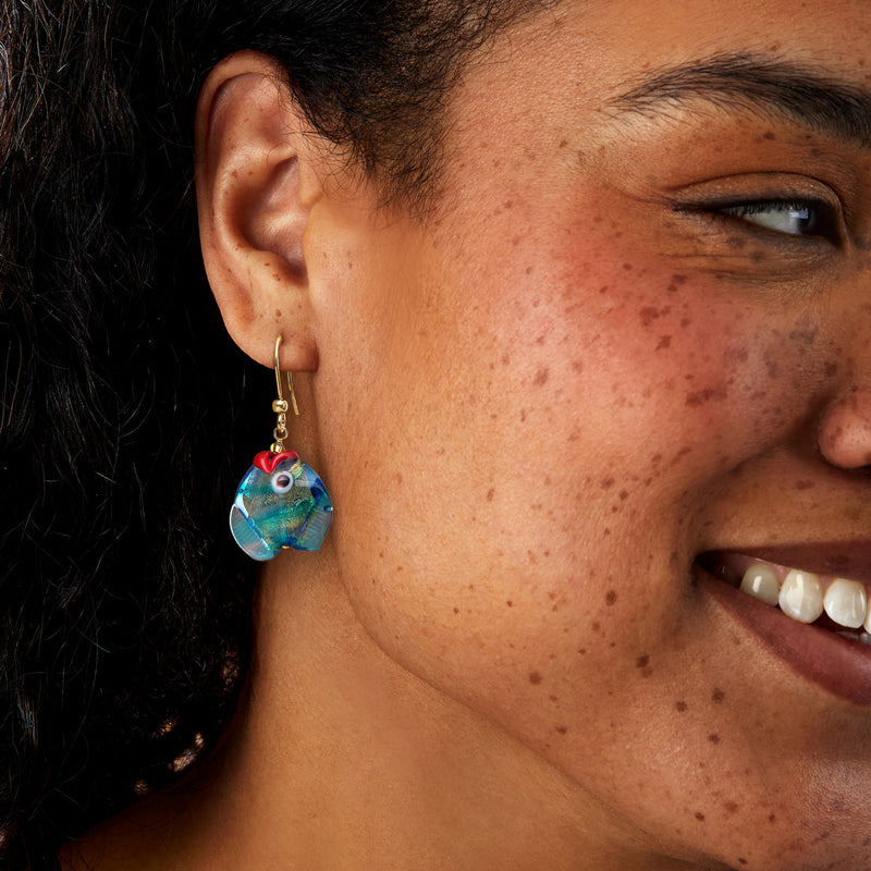 Murano glass fish drop earrings on ear, gold-tone hooks with blue-green multicolor fish