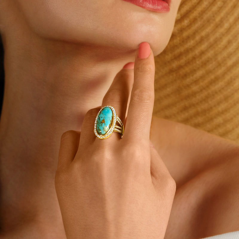 Turquoise gemstone ring on hand, framed by diamond halo in gold