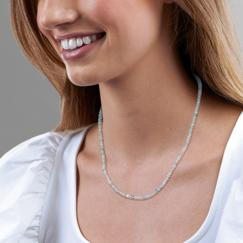 Aquamarine bead necklace on model, light blue round beads close to neckline.