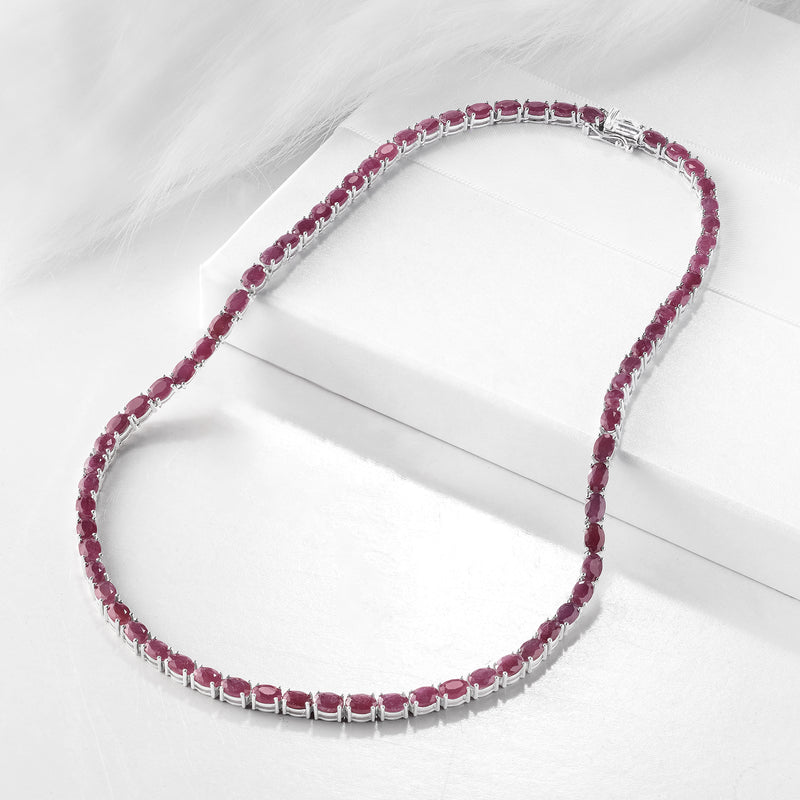 Ruby tennis necklace in sterling silver laid on a white jewelry box, oval pink stones