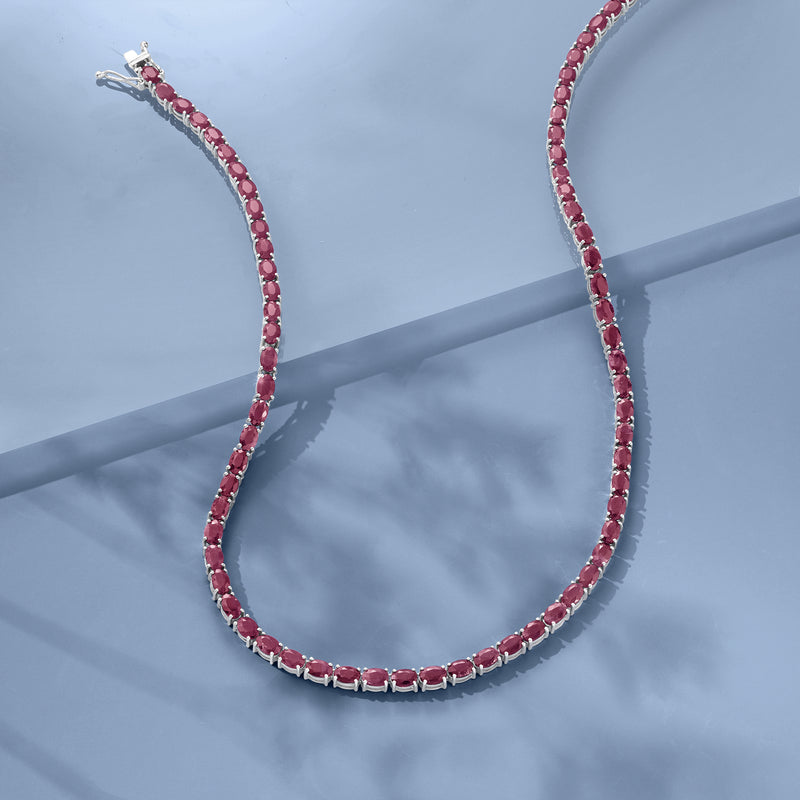 Sterling silver ruby tennis necklace with pink oval stones on a blue surface