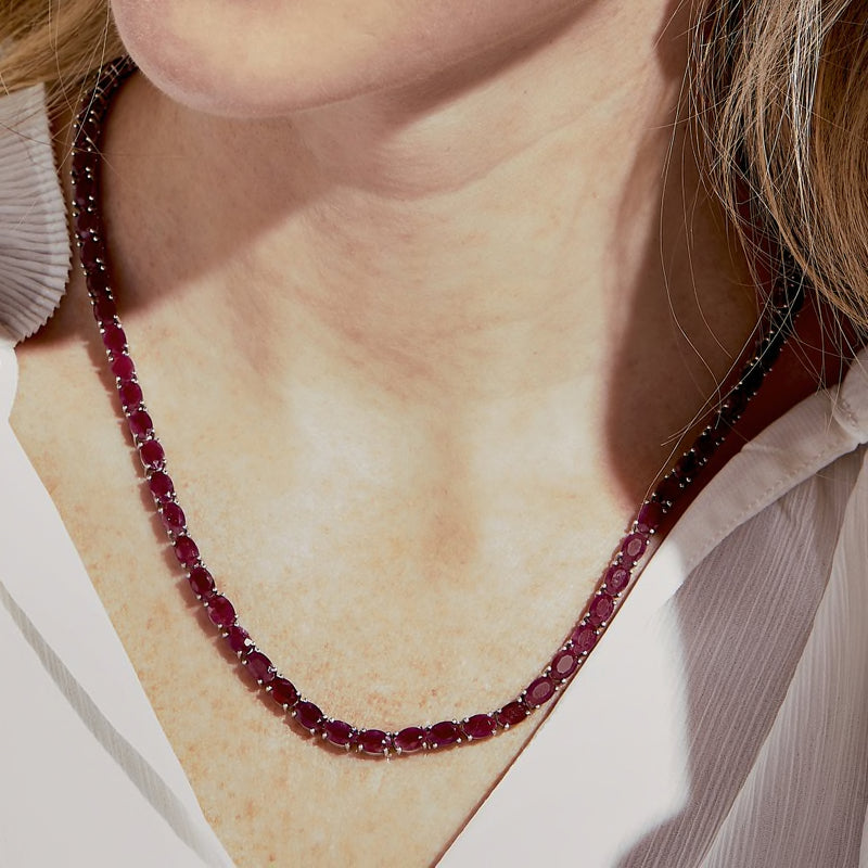 Close-up of a sterling silver ruby tennis necklace with pink oval stones at the neckline