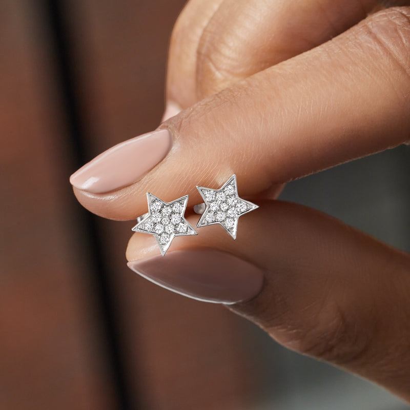 Pair of star-shaped diamond stud earrings in sterling silver on fingertips