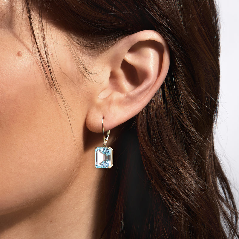 Sky blue topaz square drop earrings in 14kt yellow gold, leverback shown on ear.