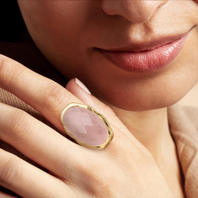 Rose quartz oval ring on finger, gold-plated bezel with faceted pale pink stone