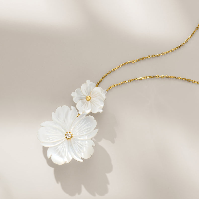 Gold chain necklace featuring two white mother-of-pearl flower pendants, side view