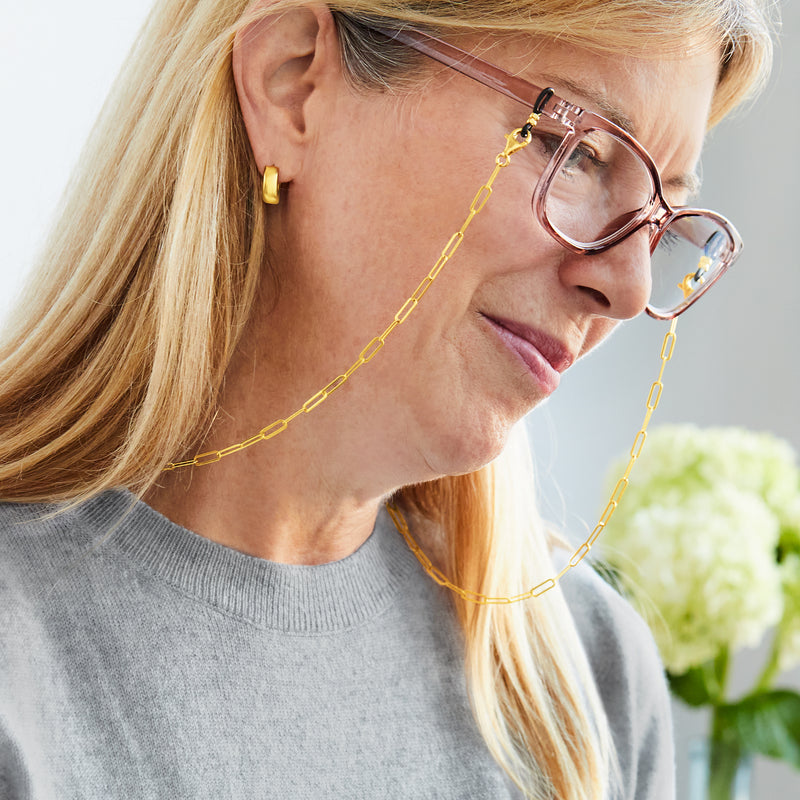 Gold paper clip link eyeglass chain draped on eyeglasses worn by woman