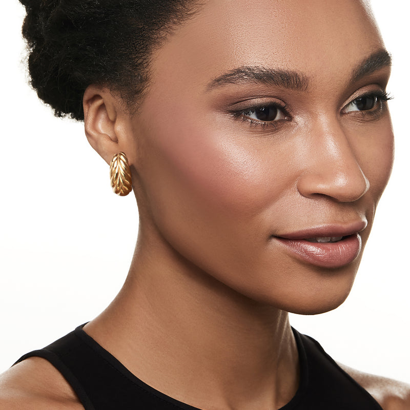 Gold-tone leaf stud earring on model, textured teardrop leaf shape