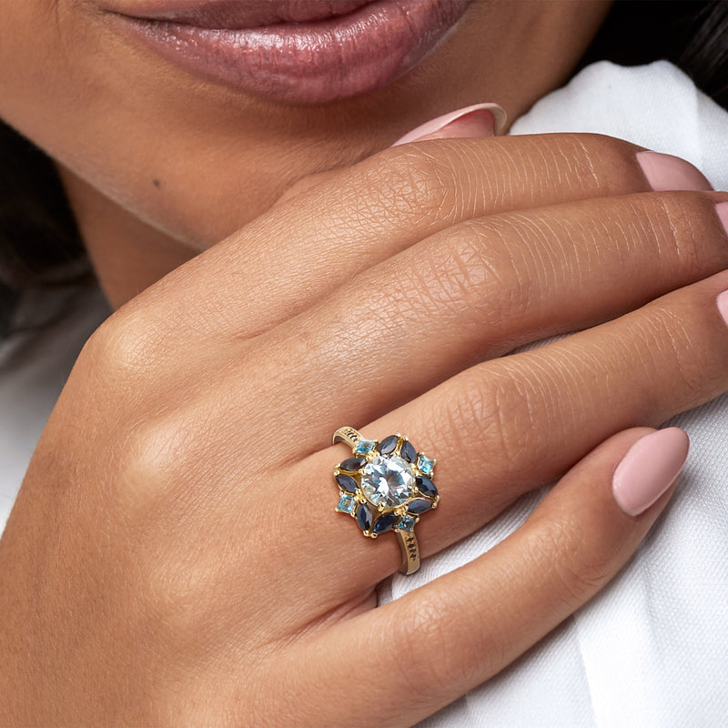 Ring on finger with sky-blue center gemstone, gold setting, and dark blue side stones