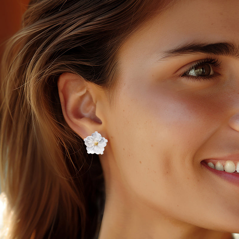 White flower drop earrings close-up on model's ear, gold posts with bright center crystals