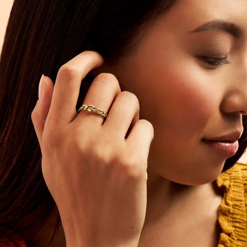 Yellow gold infinity curb-link ring on finger, polished linked infinity motif