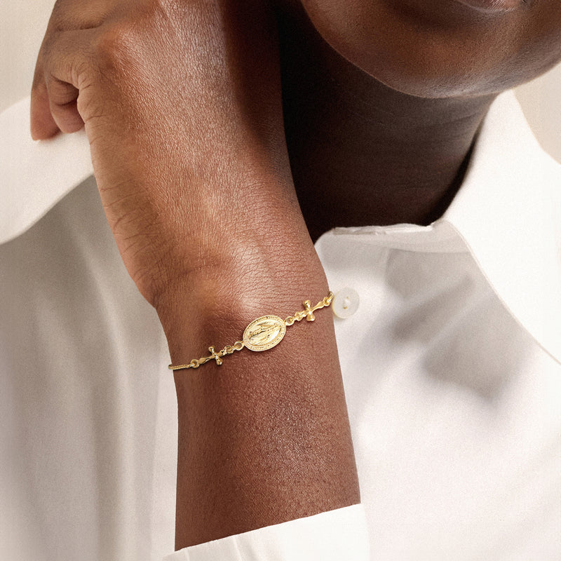 Gold-tone bolo bracelet on wrist with small oval medal charm and cross accents
