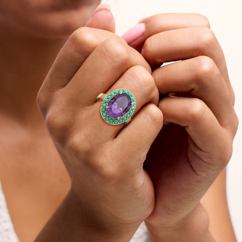 Amethyst and turquoise halo ring on hand, oval purple center with gold-tone setting