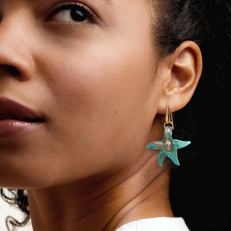 Starfish drop earrings on ear, blue-green glass star with gold-tone hoop