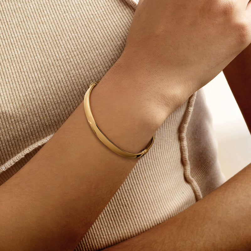 Oval gold-tone bangle bracelet worn on wrist with smooth curved profile