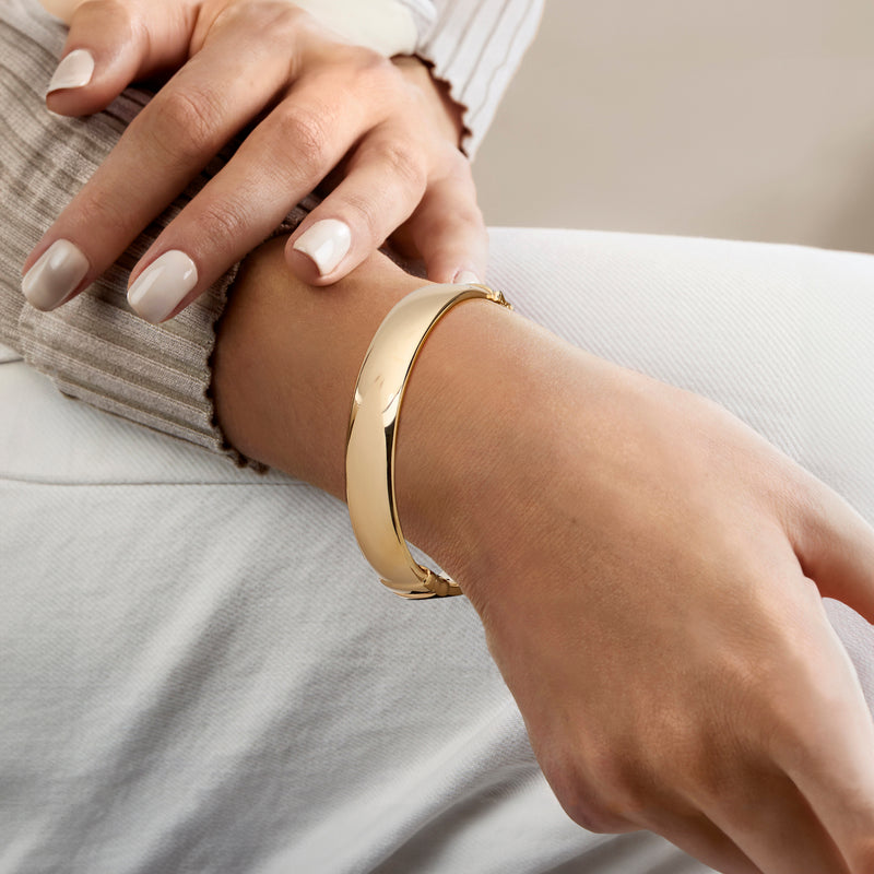 Gold-tone bangle bracelet worn on wrist with polished cuff and hinge