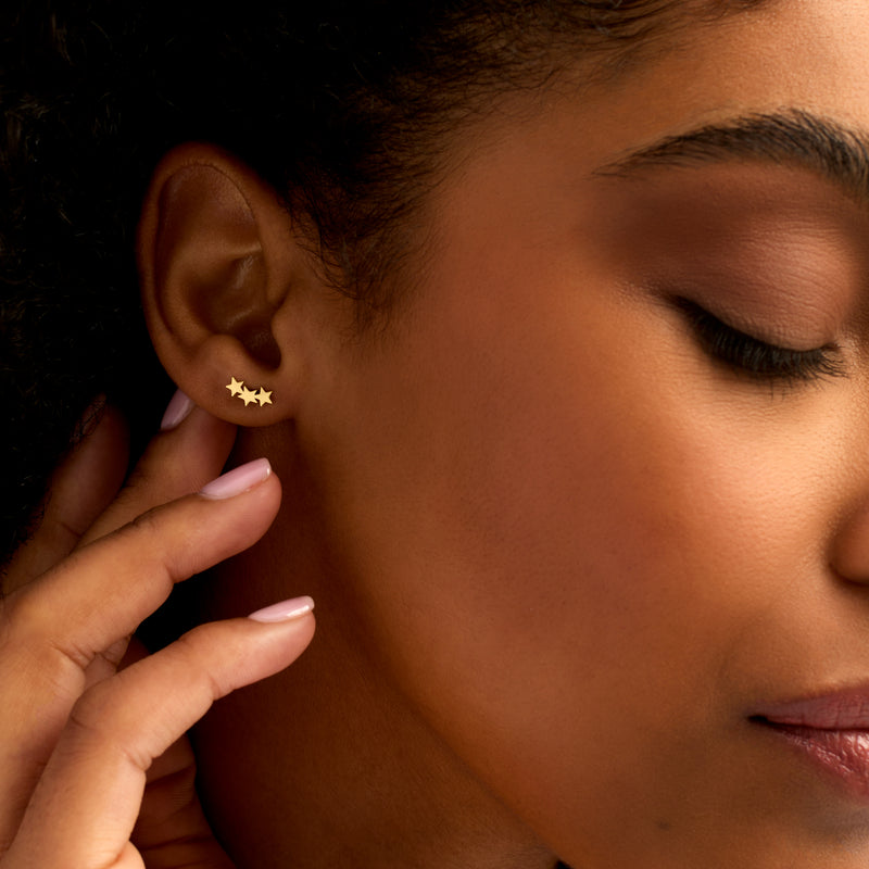 Gold star ear climber post earrings on model ear, three stacked stars