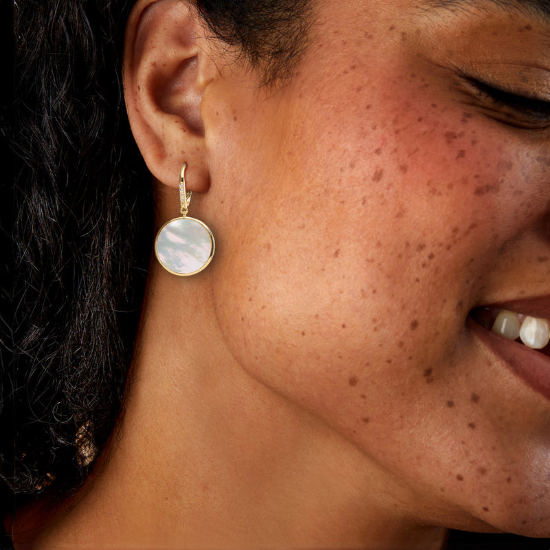 Mother-of-pearl round drop earrings on a model, gold leverback style.