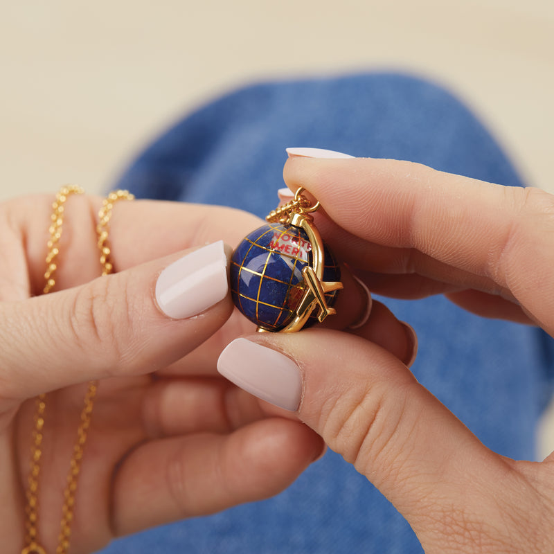 Gold globe pendant necklace held between fingers, blue map with star detail