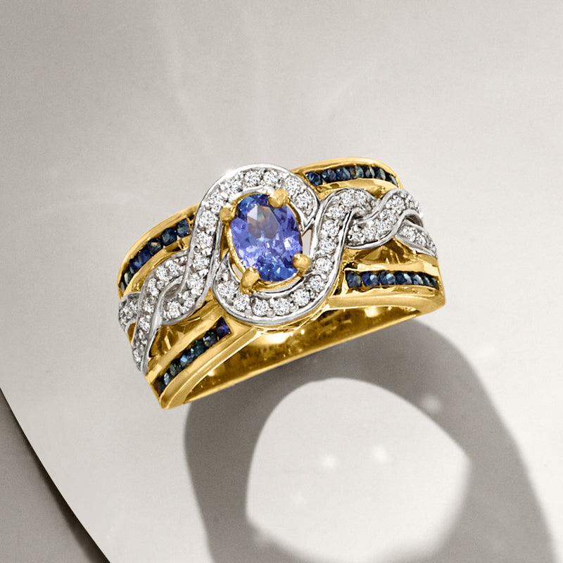 Gold-tone tanzanite ring with oval blue center stone, glittering white halo, and curved sapphire settings