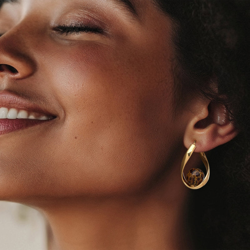 Gold hoop earrings with twisted frame and amber speckled glass bead on ear