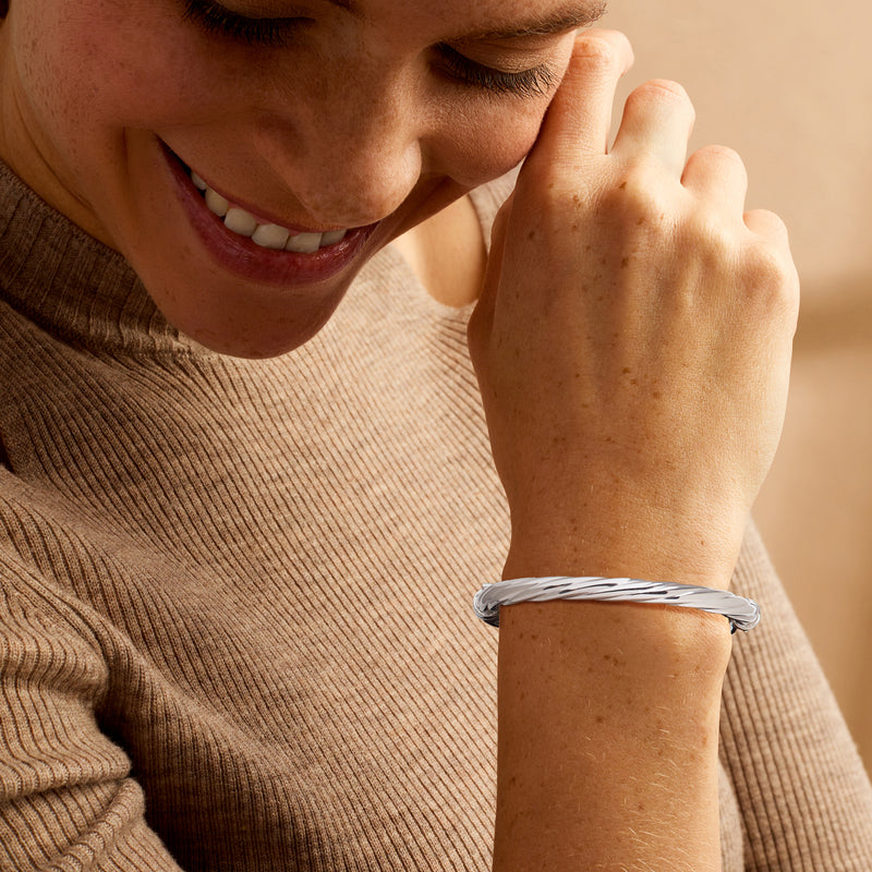 Twisted sterling silver bangle bracelet on wrist with rounded end details.
