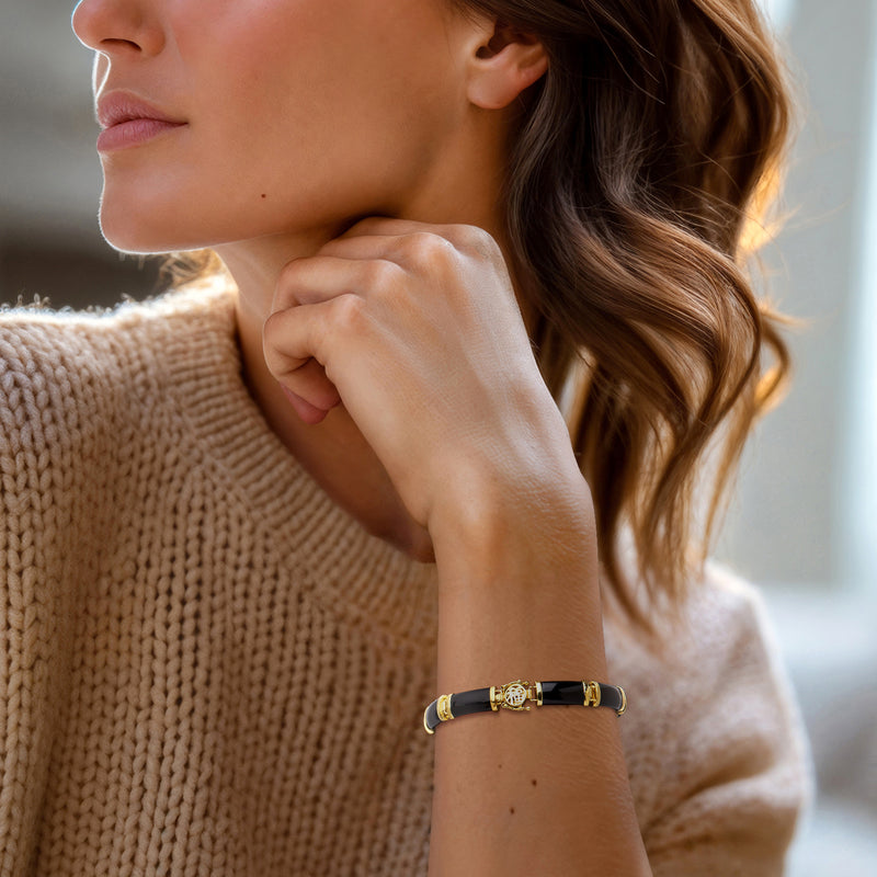 Black agate bracelet on wrist with gold-tone links and small fortune medallion charm.