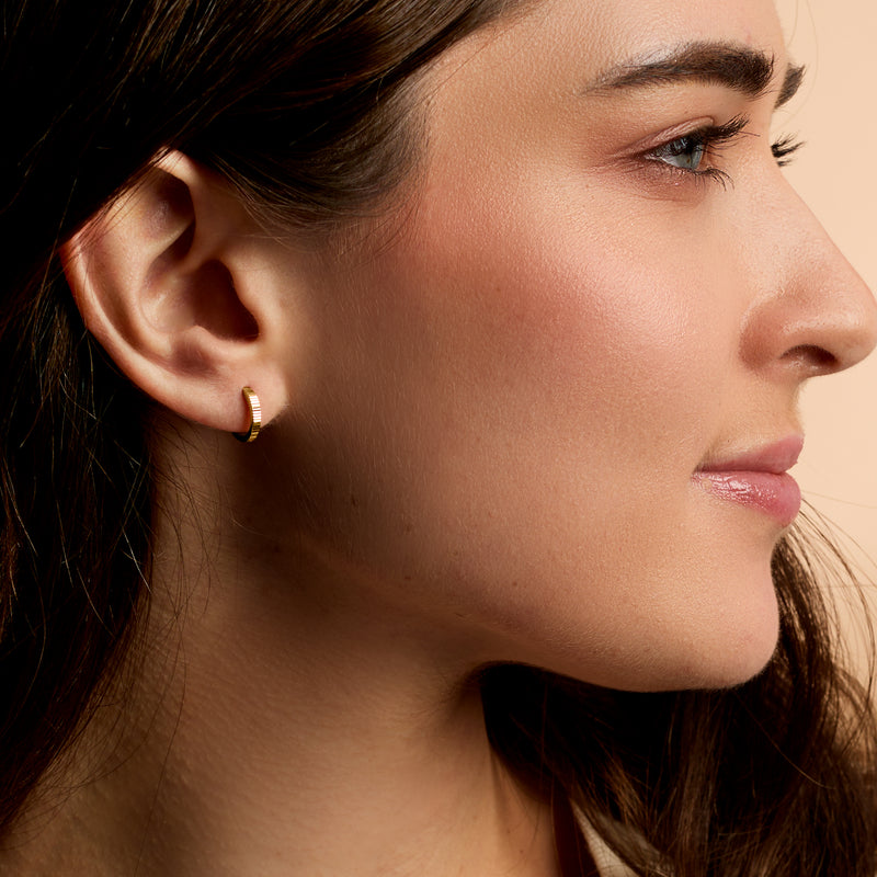 Yellow gold diamond-cut huggie hoop earrings on ear, small rounded hoops