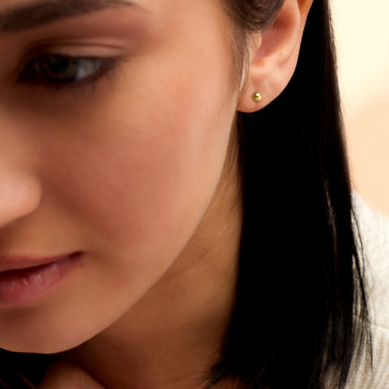Yellow gold ball stud earrings on ear, small round 3mm studs.