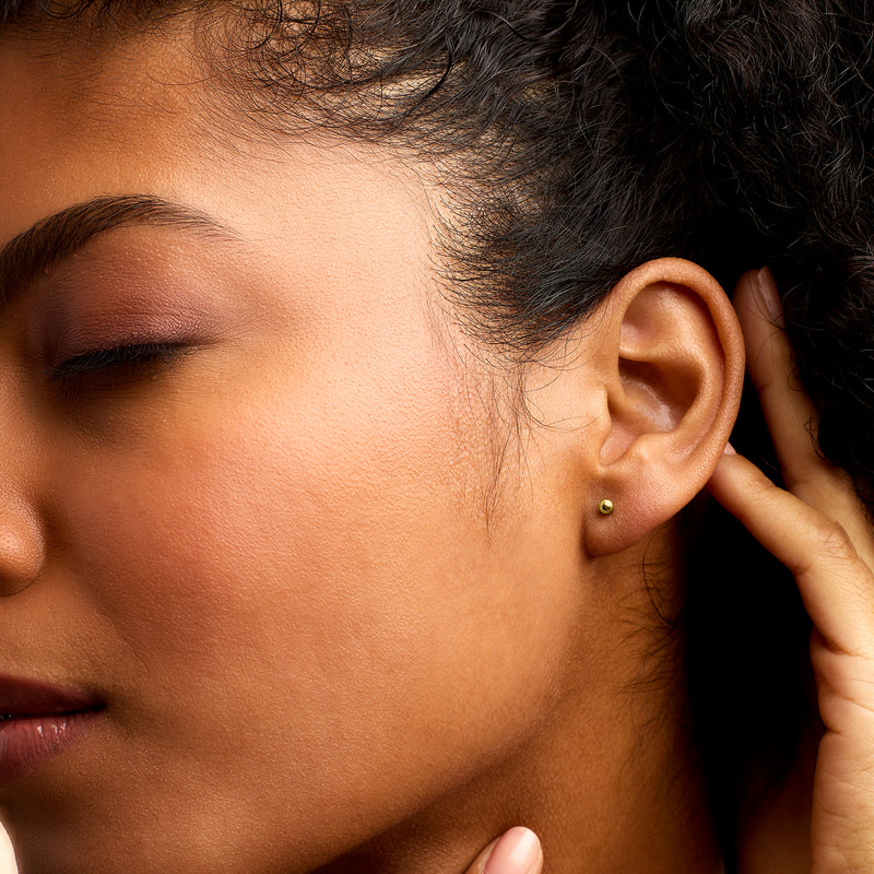 Small 3mm yellow gold ball stud earrings, visible from side on ear.